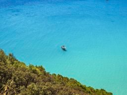Blick von der Küste von Torre delle Stelle auf das kristallklare Meer, in dem ein kleine Motorboot schwimmt Blick von der Küste von Torre delle Stelle auf das kristallklare Meer, in dem ein kleine Motorboot schwimmt